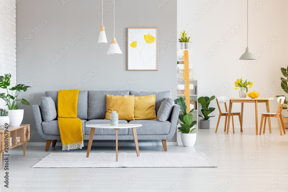 Orange blanket on grey sofa in modern apartment interior with poster and wooden table. Real photo